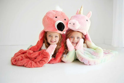 Two children wearing huggable animal hats snuggling in colorful blankets, showcasing the Huggable Unicorn design.