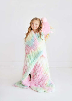 A girl wrapped in the Huggable Unicorn blanket, holding the unicorn head hood, showcasing its pastel tie-dye design.