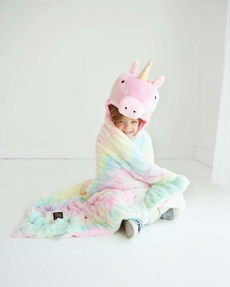 A child wearing the Huggable Unicorn blanket with a unicorn hood, featuring a colorful tie-dye design.