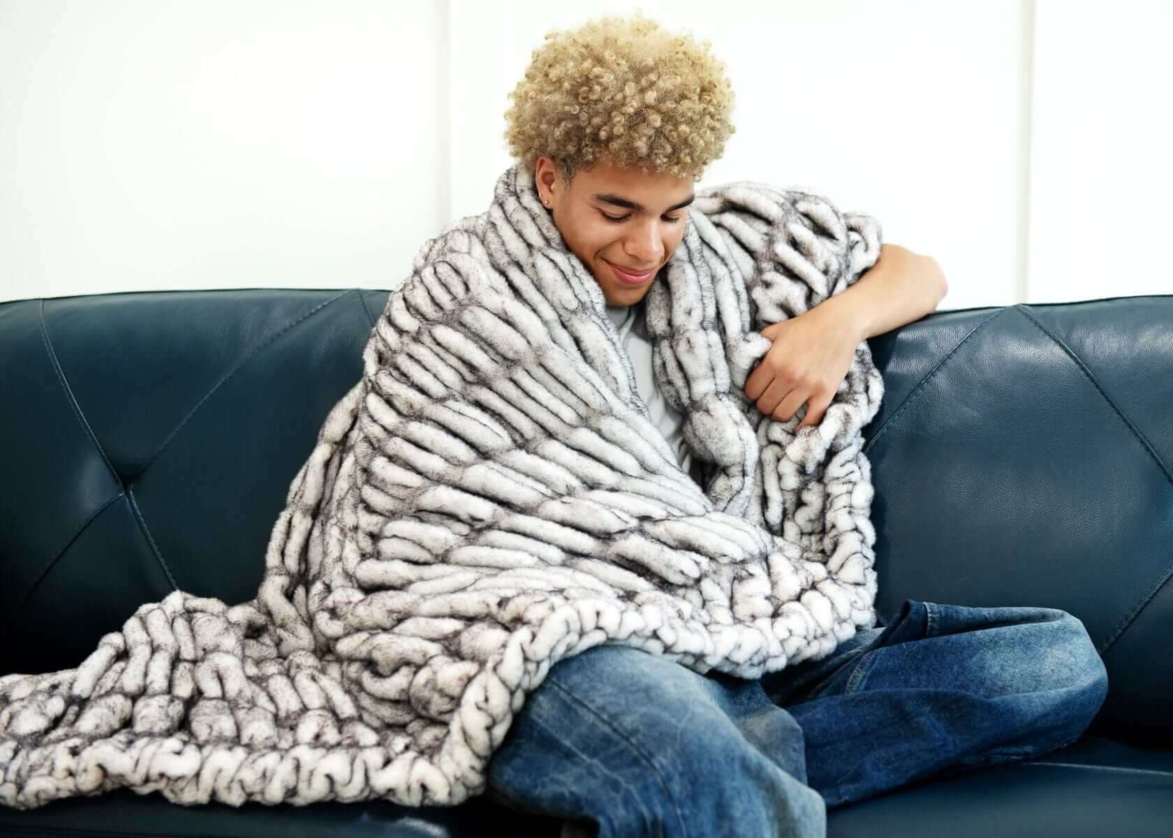 Young man enjoying warmth and comfort wrapped in the Hugs Obsidian Blanket made of soft faux fur.