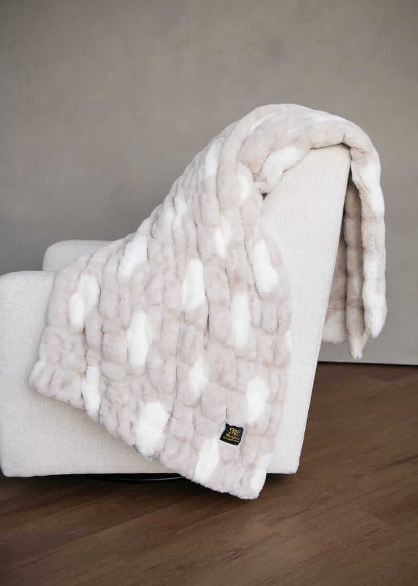 White cream and white polka dot fluffy Toasted Marshmallow blanket draped over a white chair against a gray wall.