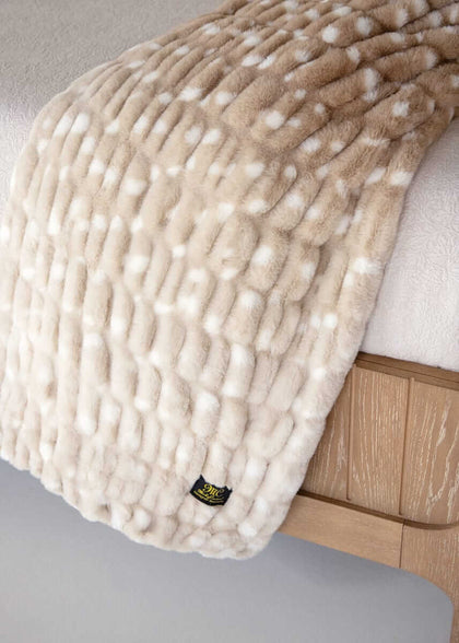 Cream-toned Minky Couture faux fur blanket with raised texture draped over a wooden bed frame.