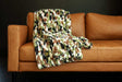 Hugs Camo Green Blanket draped over a stylish leather couch, showcasing its vibrant camo pattern.