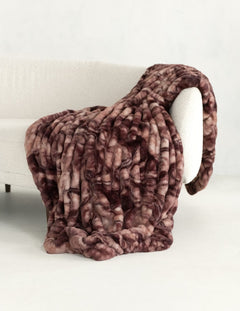 A chunky, plush faux fur throw blanket with a mottled brown and dusty rose pattern, draped over a white armchair in a minimalist room setting.