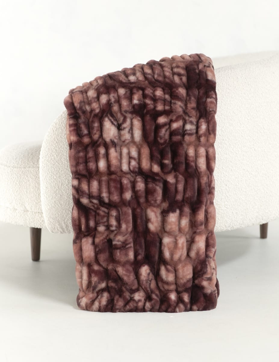 A chunky faux fur throw blanket with a marbled brown and dusty rose pattern, draped over the arm of a white boucle sofa.