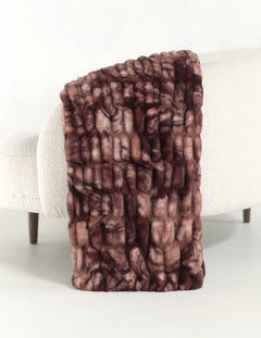 A chunky faux fur throw blanket with a marbled brown and dusty rose pattern, draped over the arm of a white boucle sofa.