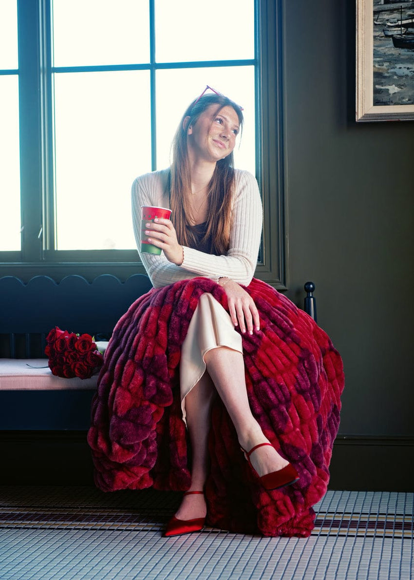 Woman sitting on a couch with a red diamond patterned blanket, holding a cup.