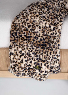 Leopard print Minky Couture faux fur throw blanket draped over a bed with brand tag visible.