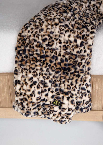 Leopard print Minky Couture faux fur throw blanket draped over a bed with brand tag visible.