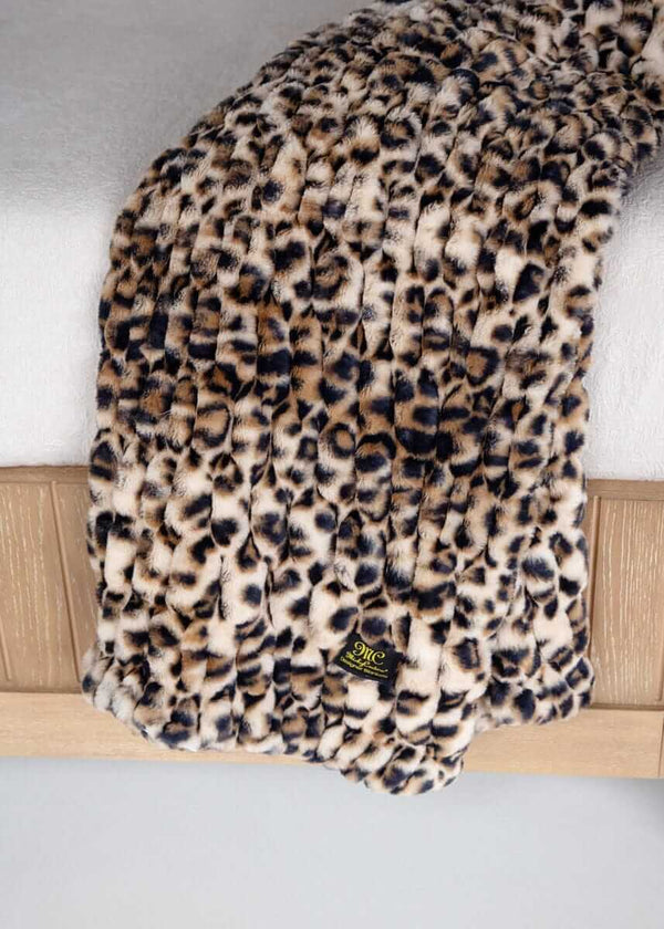 Leopard print Minky Couture faux fur throw blanket draped over a bed with brand tag visible.