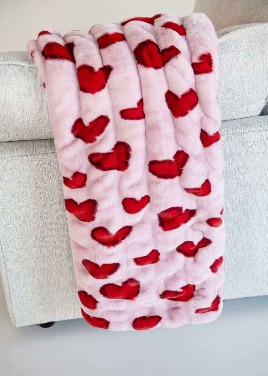Hugs Heart Red Blanket draped over a couch, featuring vibrant red hearts on a soft pink background.