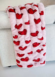 Hugs Heart Red Blanket draped over a couch, featuring vibrant red hearts on a soft pink background.