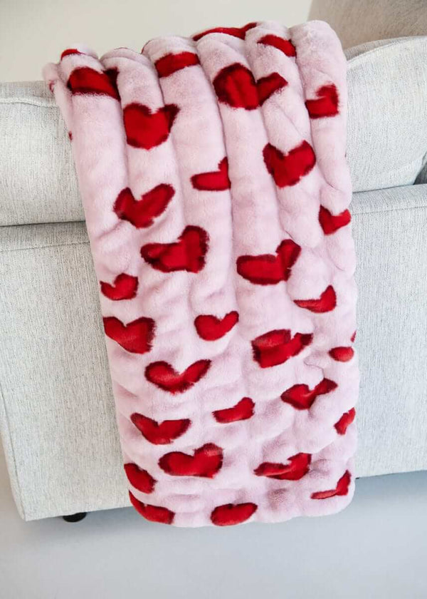 Hugs Heart Red Blanket draped over a couch, featuring vibrant red hearts on a soft pink background.