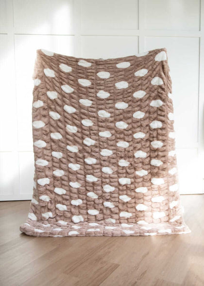 Fluffy brown and white polka dot patterned blanket hanging on a wooden floor and white wall.
