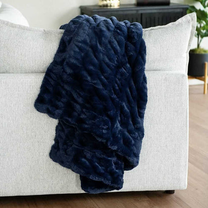Navy blue Minky Couture weighted blanket draped over a light gray sofa, showing its soft textured fabric.