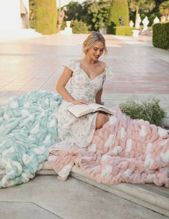 A woman reading a book while seated on the Minky Couture Hugs Polka Dot Tiffany Blanket in Tiffany blue and a pink blanket.