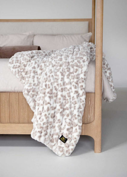 Minky Couture faux fur throw blanket with a soft animal-inspired pattern draped over a wooden bed frame.
