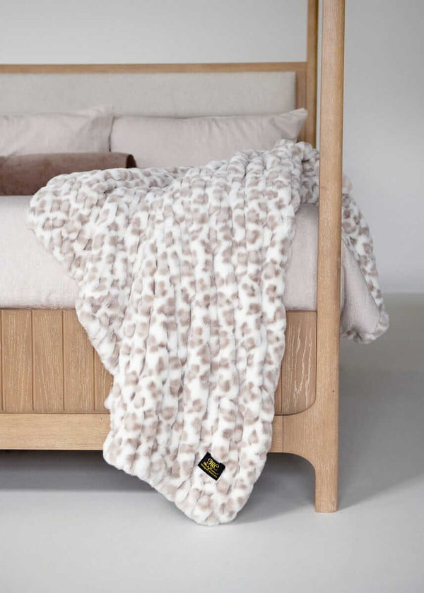 Minky Couture faux fur throw blanket with a soft animal-inspired pattern draped over a wooden bed frame.