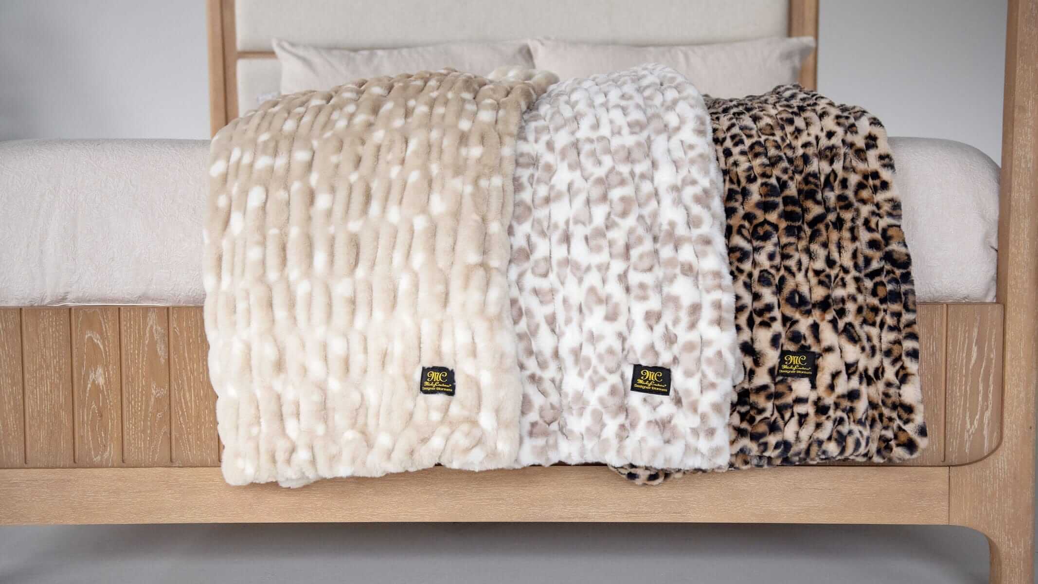Three Minky Couture plush throw blankets in neutral and animal-inspired textures draped over a bed.