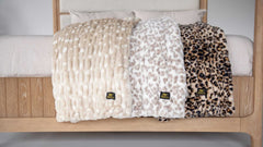 Three Minky Couture plush throw blankets in neutral and animal-inspired textures draped over a bed.