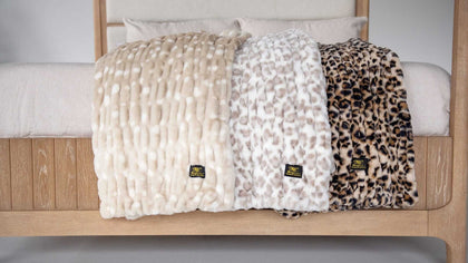 Three Minky Couture plush throw blankets in neutral and animal-inspired textures draped over a bed.