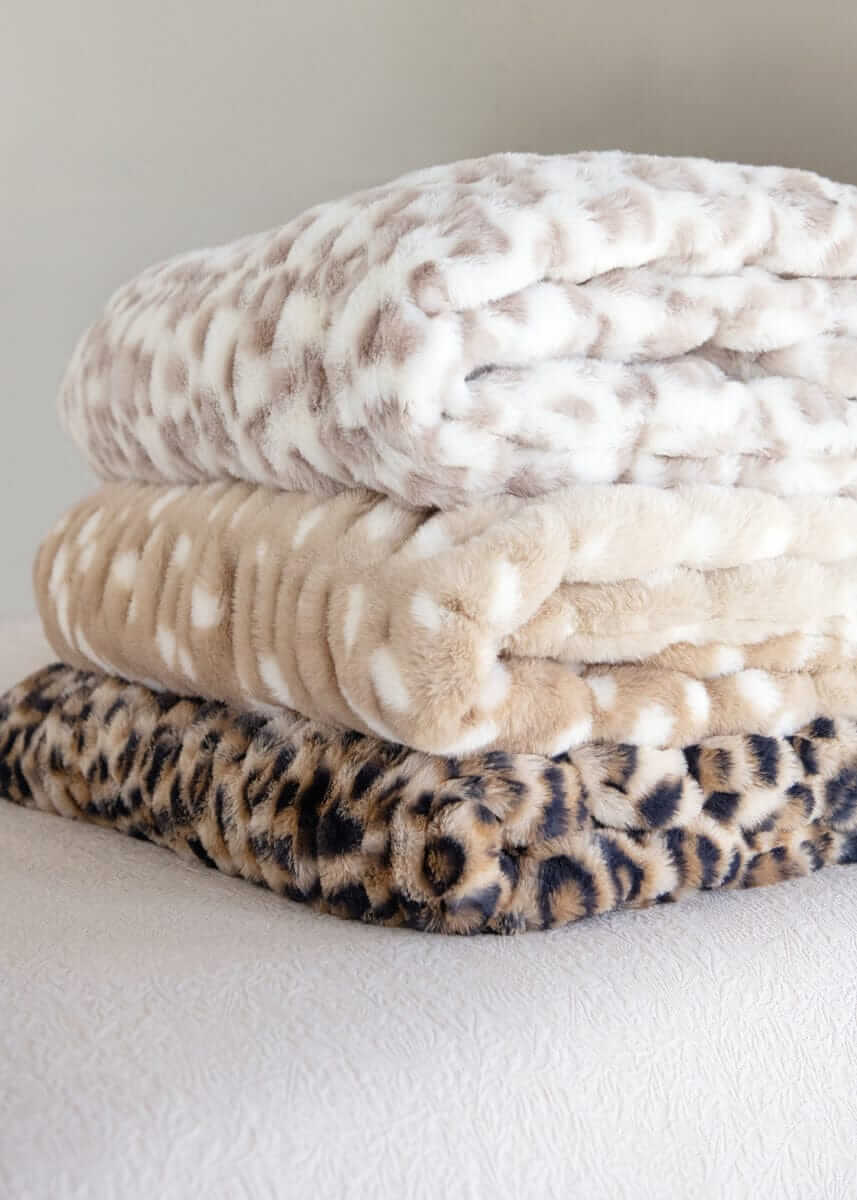 Stack of three Minky Couture faux fur blankets in snow leopard, tan spotted, and leopard prints.