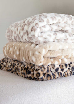 Stack of three Minky Couture faux fur blankets in snow leopard, tan spotted, and leopard prints.