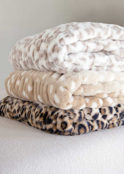 Stack of three Minky Couture faux fur blankets in snow leopard, tan spotted, and leopard prints.