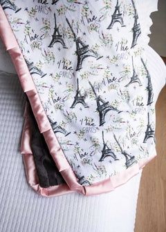 Folded fabric with Eiffel Tower and 'I love Paris' text pattern on a bed.