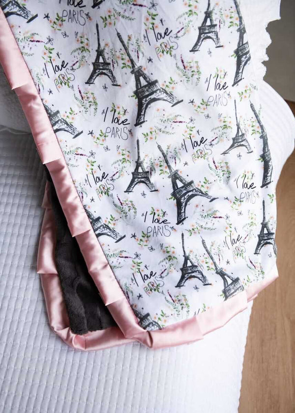 Folded fabric with Eiffel Tower and 'I love Paris' text pattern on a bed.