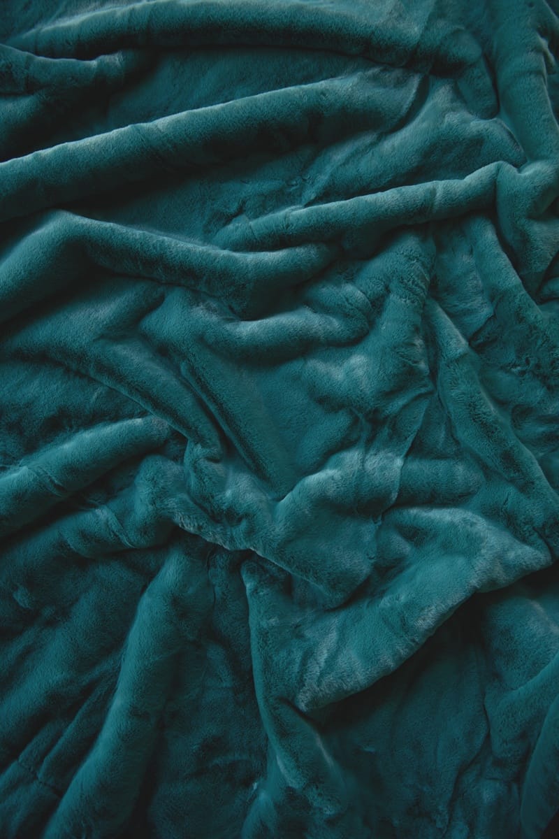 A close-up of a plush, textured fabric in a deep teal color, shown with soft folds and ripples.