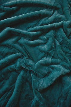 A close-up of a plush, textured fabric in a deep teal color, shown with soft folds and ripples.