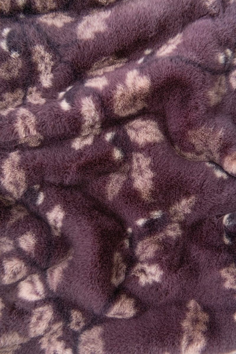 Close-up of a plush faux fur fabric with a mottled pattern in dark purple and light beige.