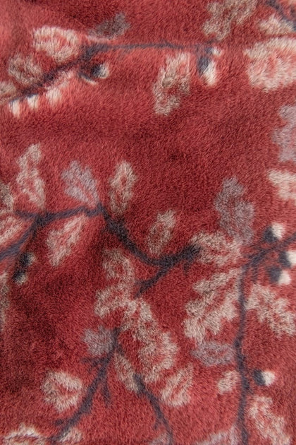 A close-up of a plush, textured fabric with a dusty red base and a light beige and dark floral branch pattern.