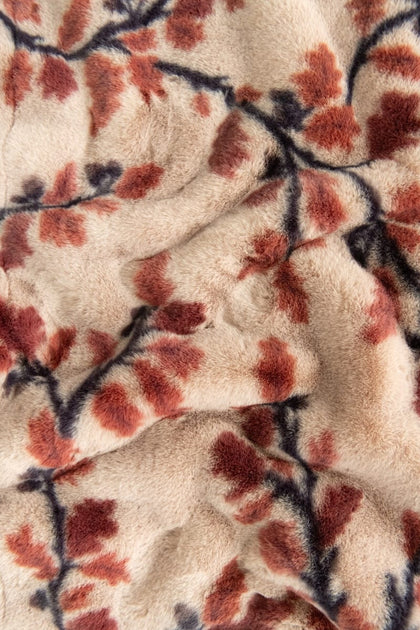Close-up of a plush blanket with a branch and leaf pattern in rust red and dark navy on a warm beige background.