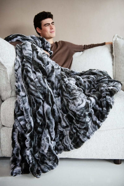 Cozy style featuring the Hugs Marble Onyx Blanket draped over a sofa with a relaxed man enjoying its warmth.