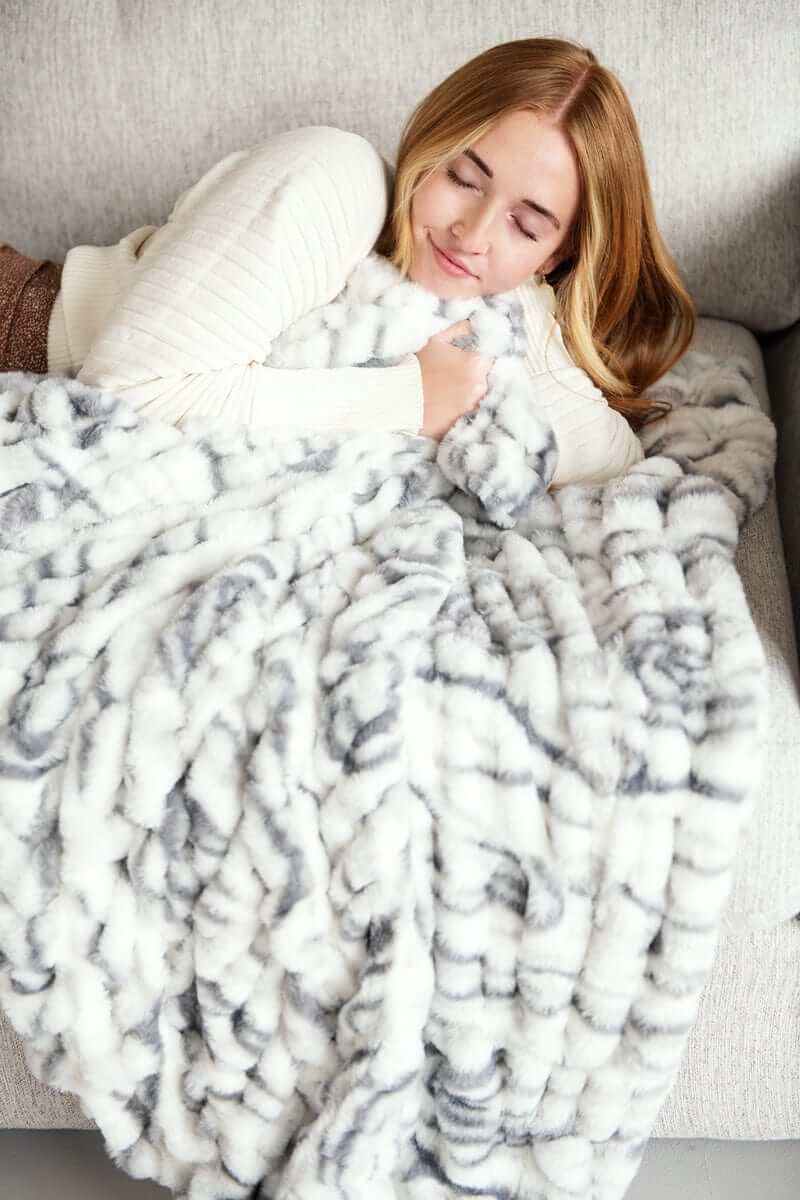 Cozy woman wrapped in Hugs Marble Pewter Blanket, showcasing plush design and elegant marble print.