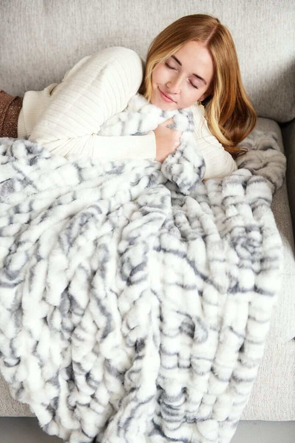 Cozy woman wrapped in Hugs Marble Pewter Blanket, showcasing plush design and elegant marble print.