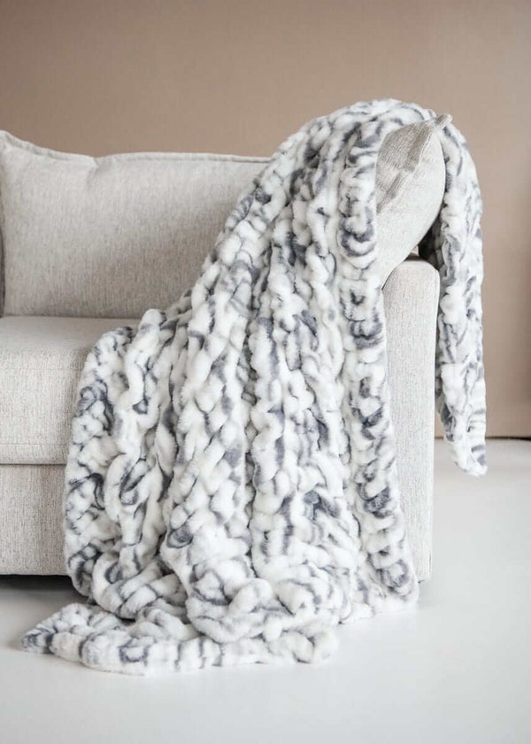 Hugs Marble Pewter Blanket draped over a cozy couch, showcasing modern elegance with a plush marble design.