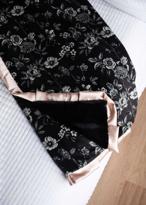 Black Moody floral-patterned fabric with champagne satin trim on a white bed.