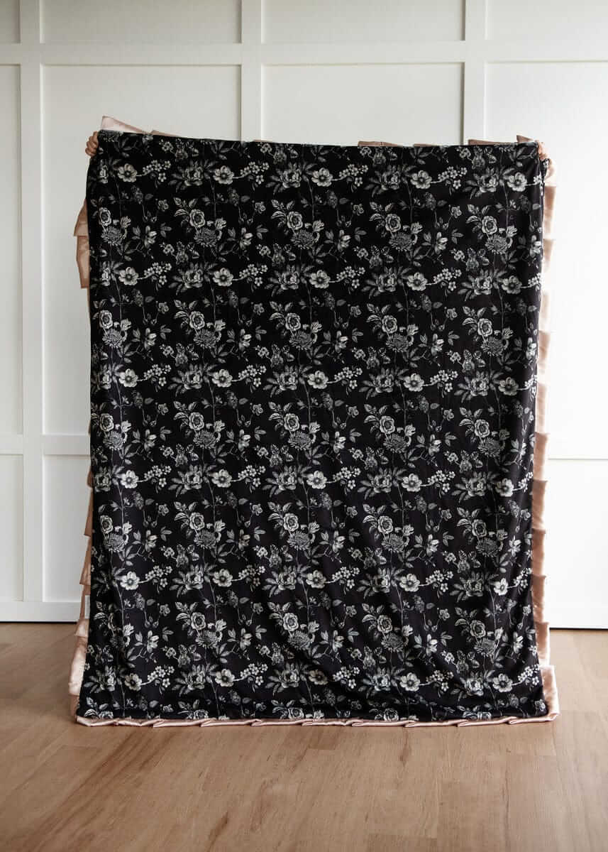 Black Moody floral patterned fabric on a wooden surface with a white paneled wall background.