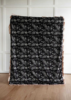 Black Moody floral patterned fabric on a wooden surface with a white paneled wall background.