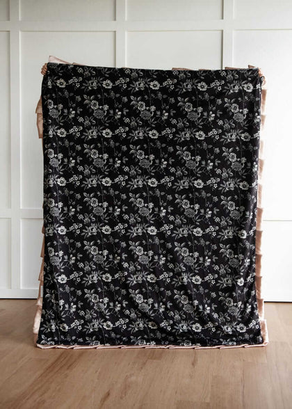 Black Moody floral patterned fabric on a wooden surface with a white paneled wall background.