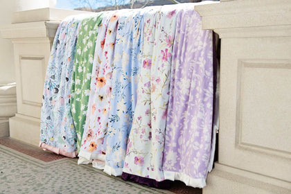 Minky Couture floral blankets displayed outdoors, each featuring vibrant colors and delicate flower patterns.