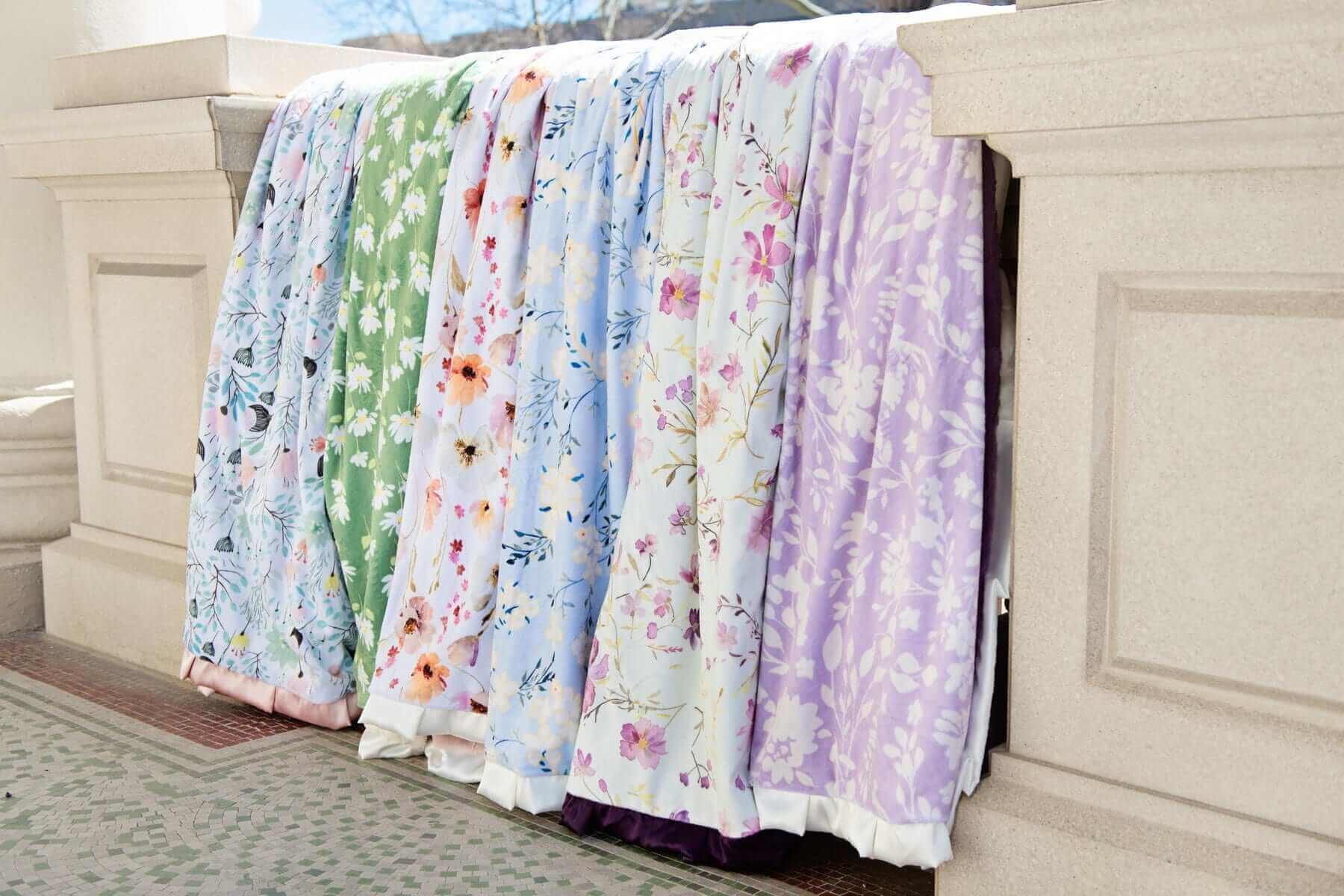 Minky Couture floral blankets displayed outdoors, each featuring vibrant colors and delicate flower patterns.