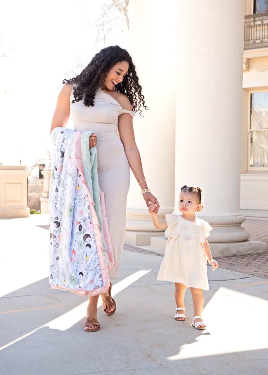 A mother and child blissfully walking with a Spring Wildflower Blanket draped over the mother's arm outdoors.