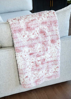 Sandra Plush Pink Minky Couture blanket in soft pink draped over a light sofa, showing its textured, cozy fabric.
