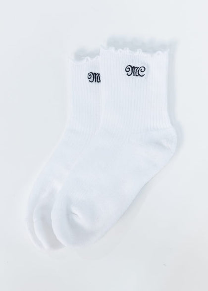 A pair of white ribbed ankle socks with scalloped edges and black embroidered MC Minky Couture lettering on the cuffs, displayed on a clean white background.