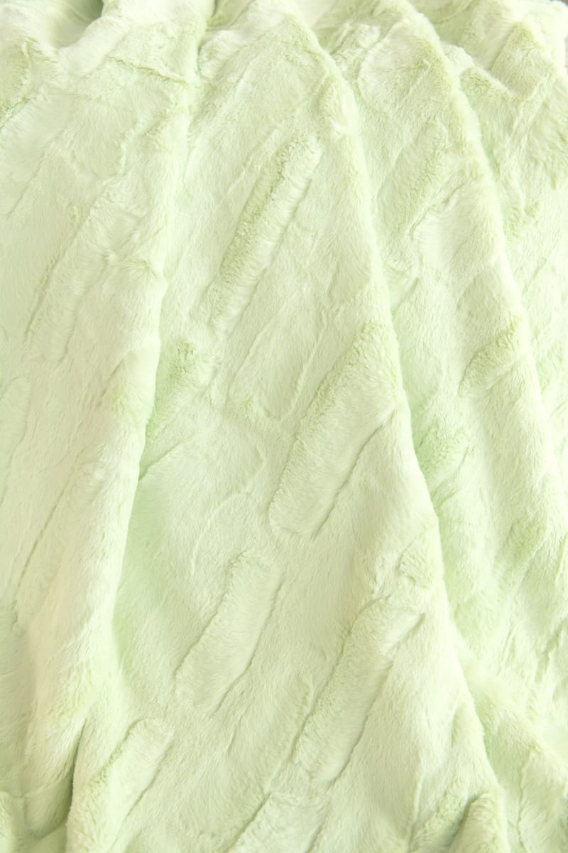 A close-up of a pale mint green Minky Couture Sorbet Lemon Lime faux fur fabric with soft, crinkled vertical folds.