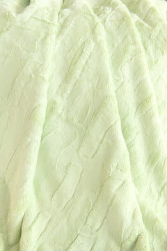 A close-up of a pale mint green Minky Couture Sorbet Lemon Lime faux fur fabric with soft, crinkled vertical folds.